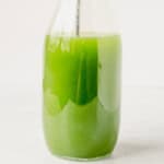 stirring a cucumber margarita in a glass pitcher.