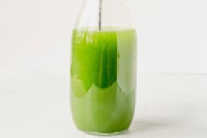 stirring a cucumber margarita in a glass pitcher.