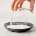 dipping a rocks glass into margarita salt on a black plate.