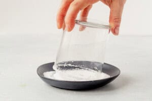 dipping a rocks glass into margarita salt on a black plate.