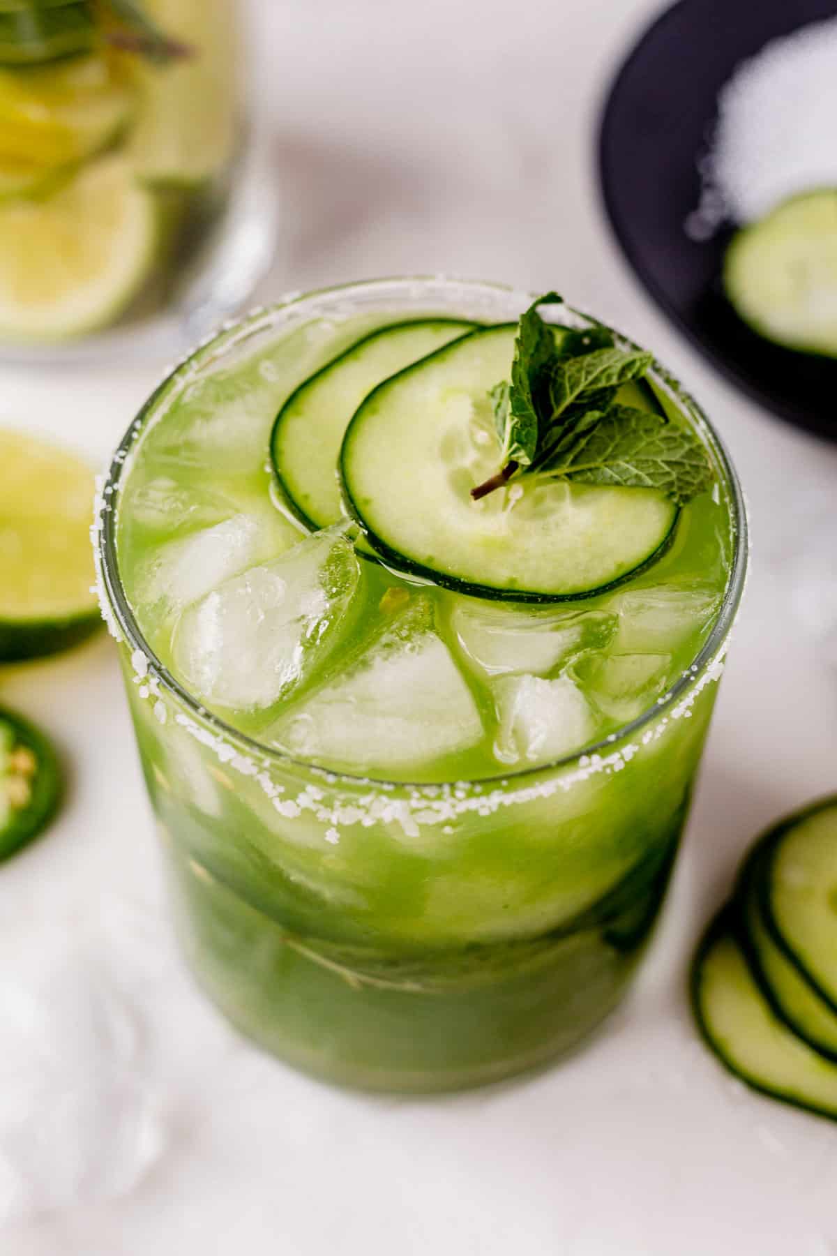 a cucumber margarita in a glass with fresh cucumber slices and mint