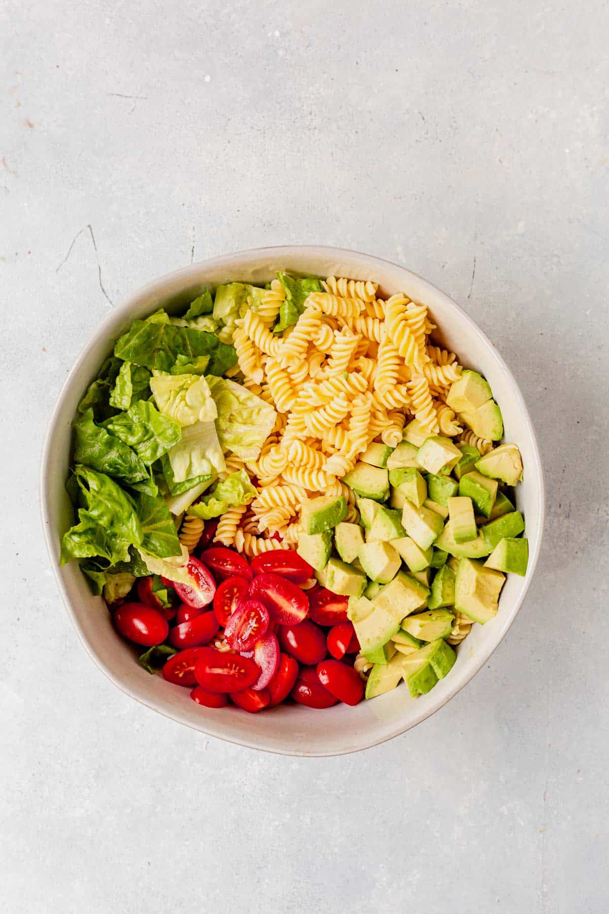 pasta, lettuce, toamto, avocado in a bowl