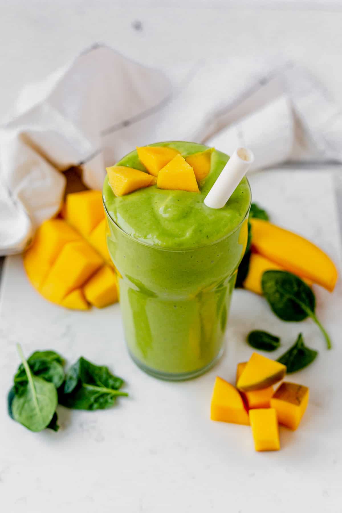 mango spinach smoothie in a glass with a straw