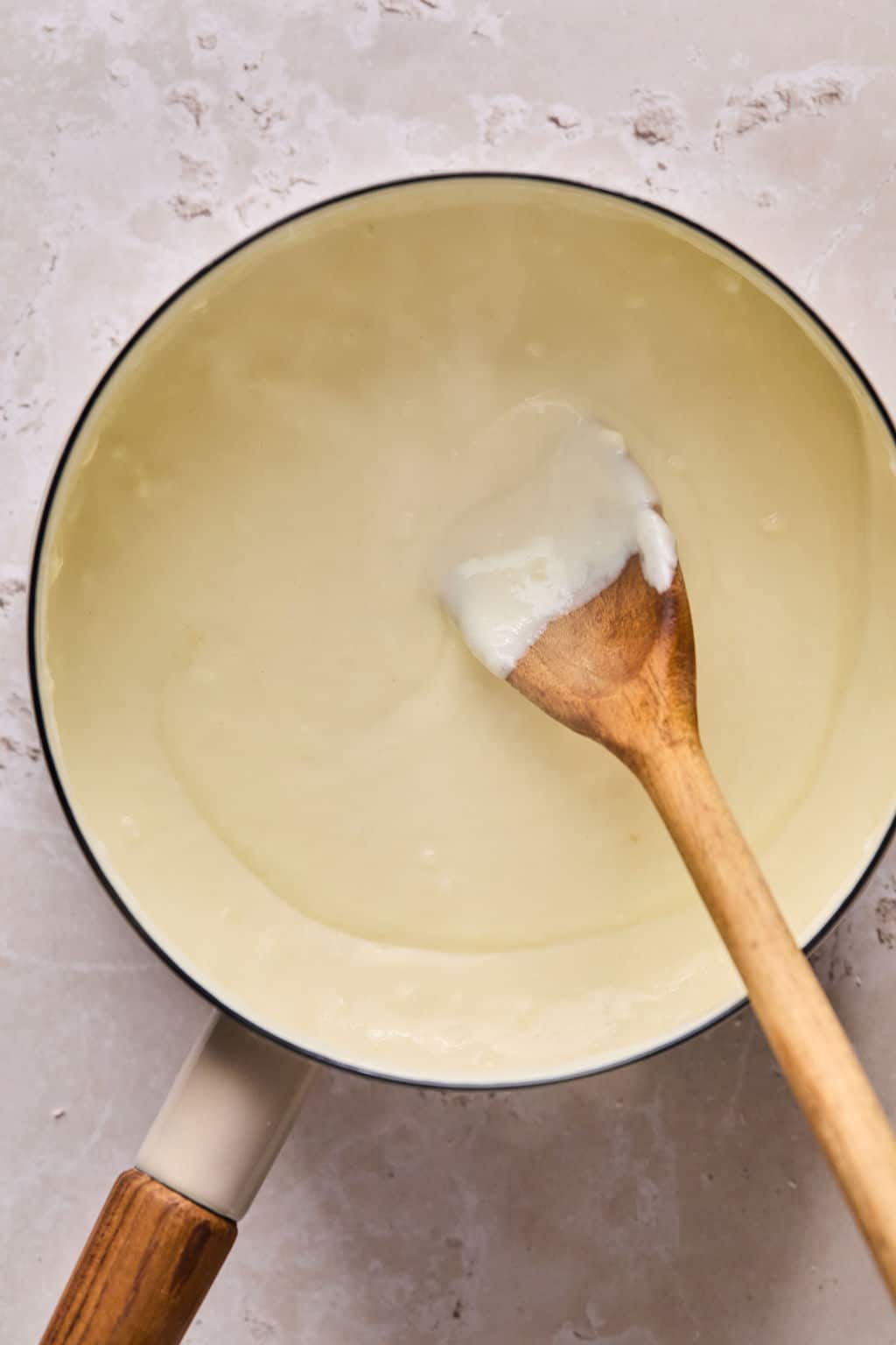 homemade alfredo sauce in a saucepan with a wooden spoon.