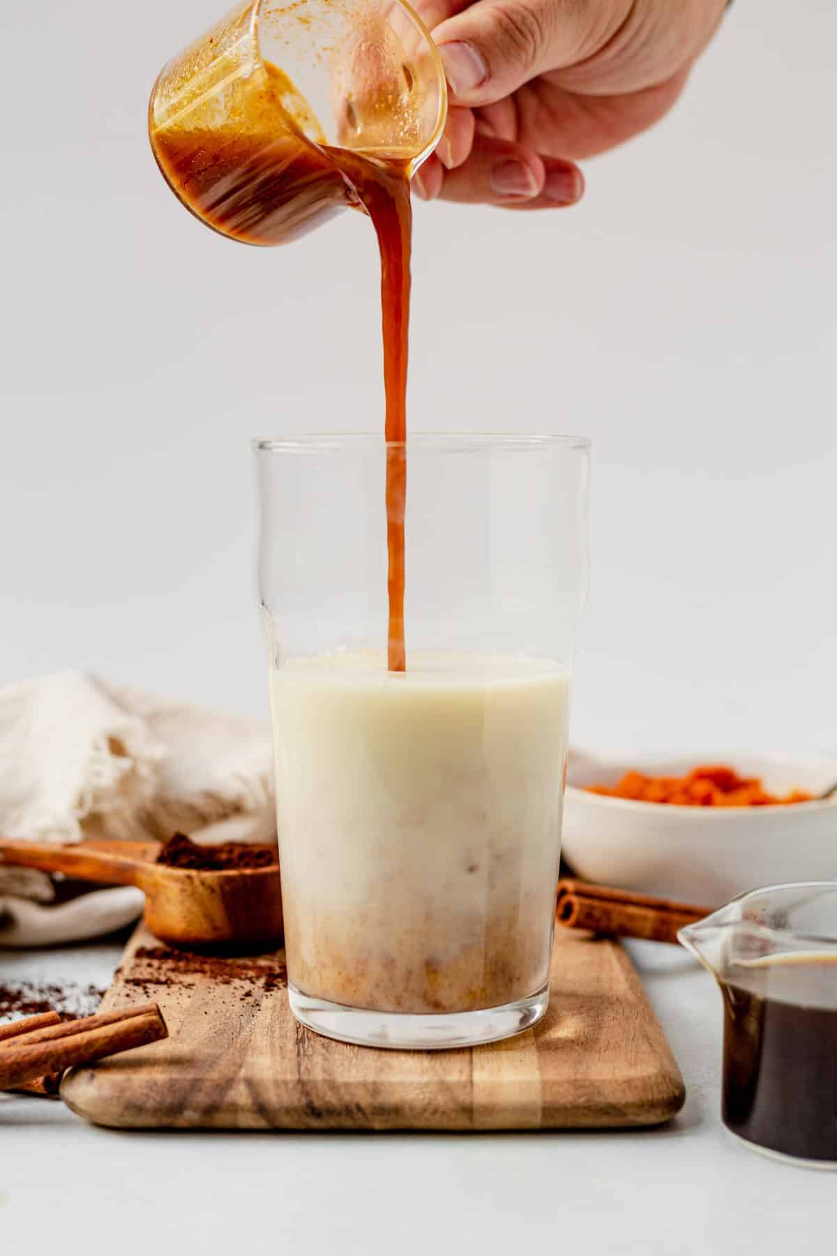 pouring pumpkin spice syrup in to a glass of milk.