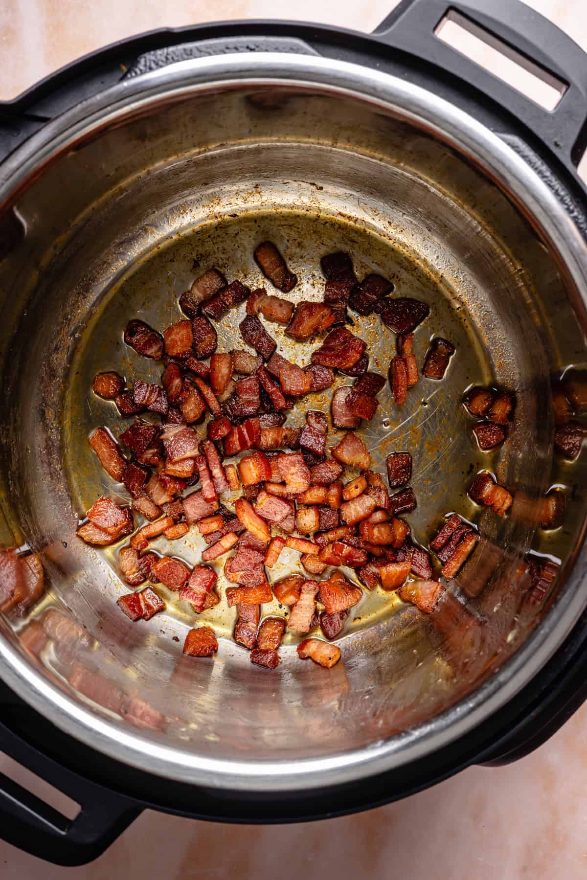 Crispy, browned bacon pieces at the bottom of a stainless steel Instant Pot, ready to add rich flavor to your instant pot corn chowder, viewed from above on a light-colored surface.