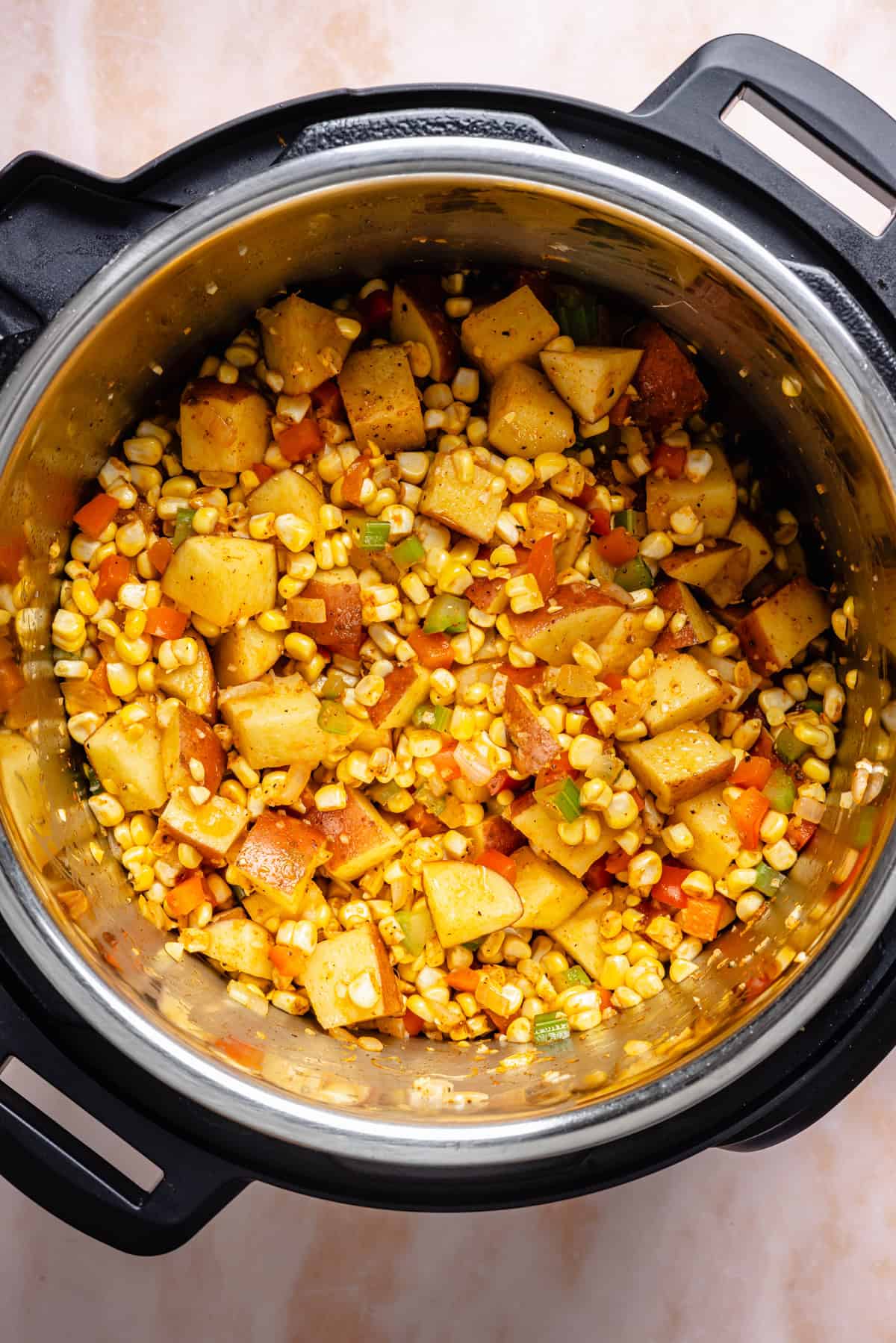 Chopped potatoes, corn, carrots, and green beans mixed with spices in an Instant Pot, ready to be cooked into a hearty instant pot corn chowder.