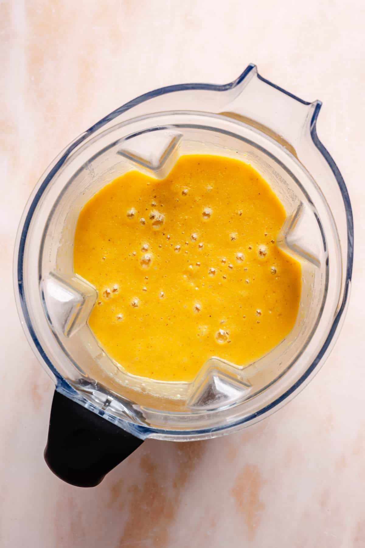 Top view of a blender filled with a thick, frothy yellow-orange liquid—perfect for preparing instant pot corn chowder—on a light, textured surface.