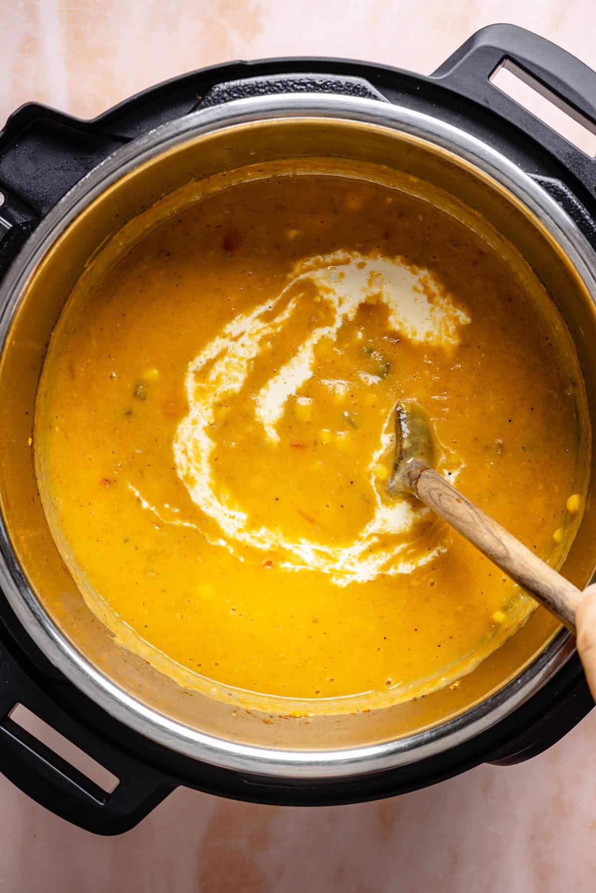 A hand stirs a thick, creamy instant pot corn chowder with cream swirled in, inside an Instant Pot on a light countertop.