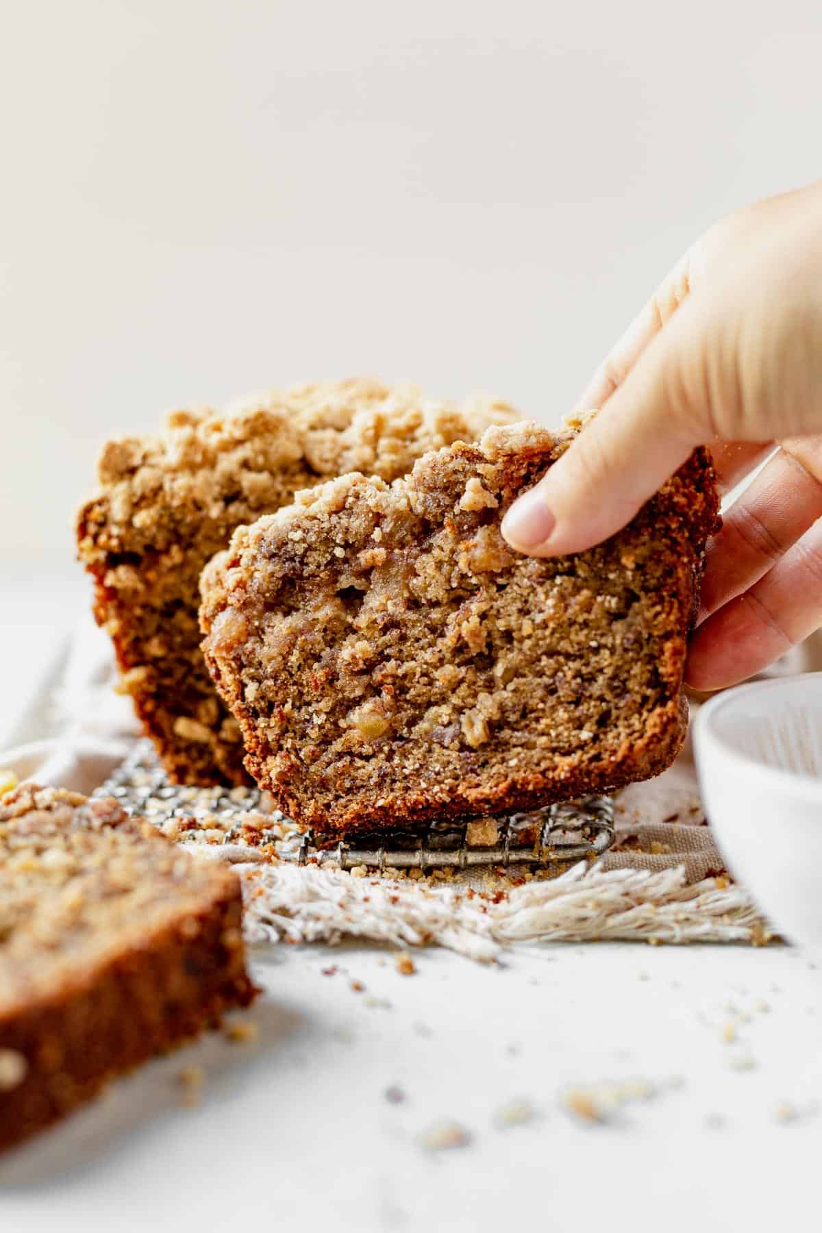 a hand picking up a slice of apple banana bread from the loaf