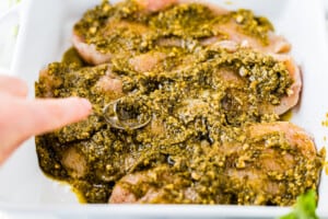 spreading pesto on top of chicken in a baking dish