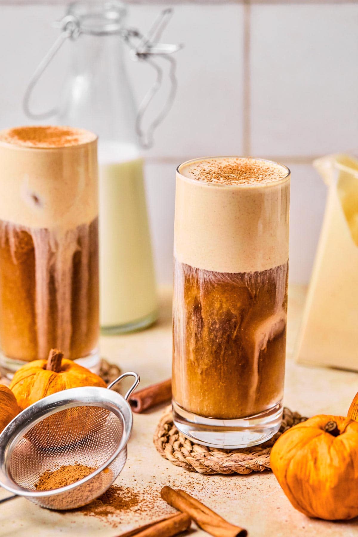 two glasses of pumpkin cream cold brew on a wood coasters dusted with pumpkin pie spice.