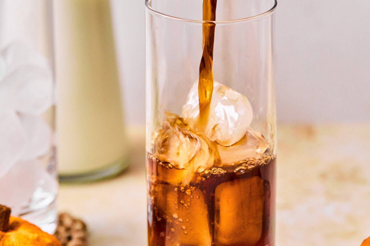 pouring cold brew coffee into a tall glass with ice.