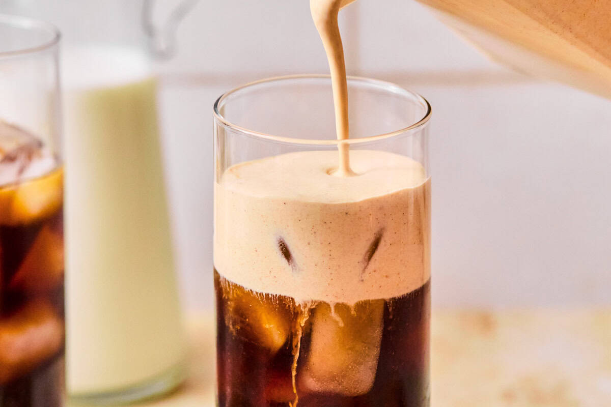 pouring pumpkin cream on top of cold brew in a glass with ice.