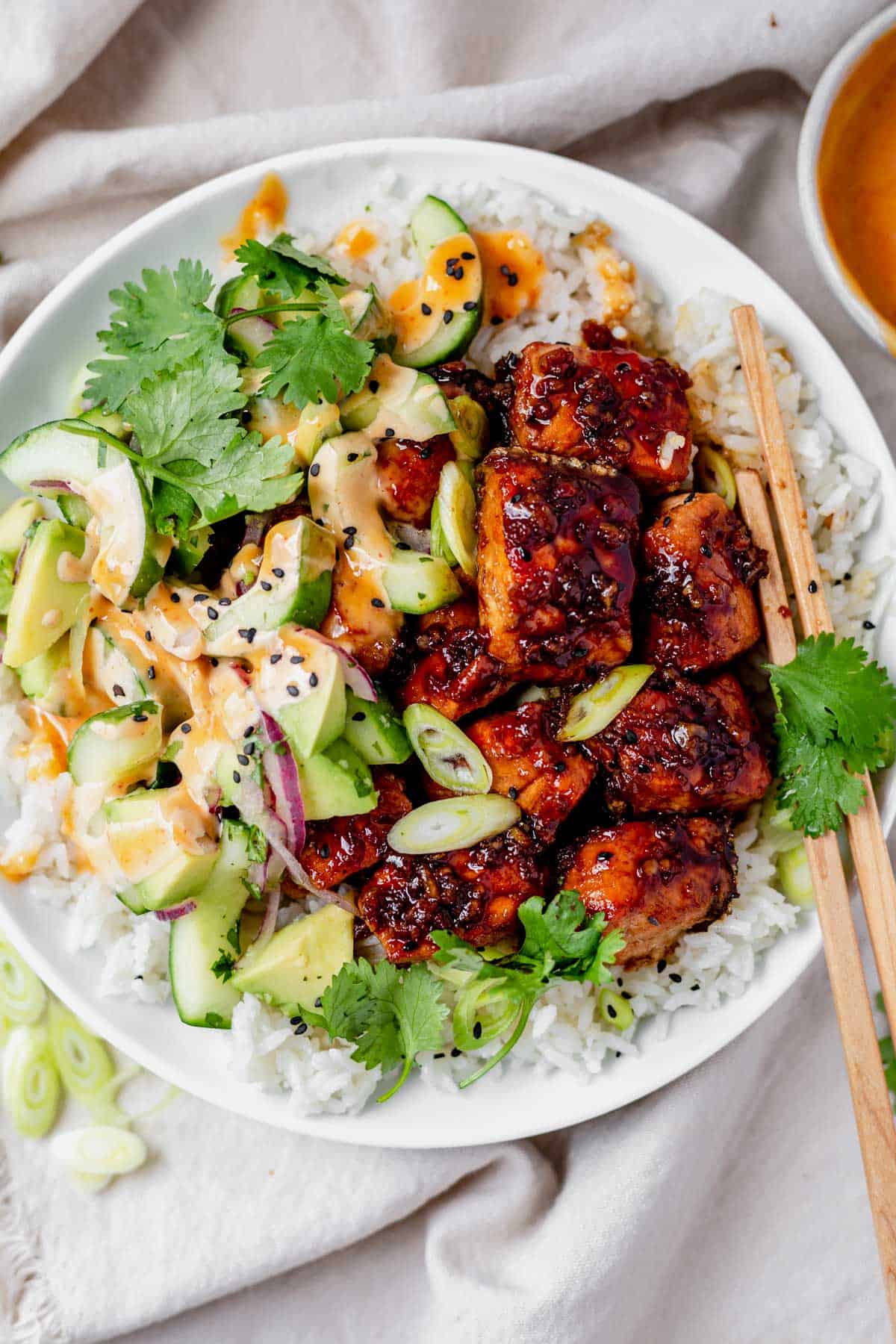 a white bowl with coconut rice, cucumber avocado salad and honey garlic salmon bites