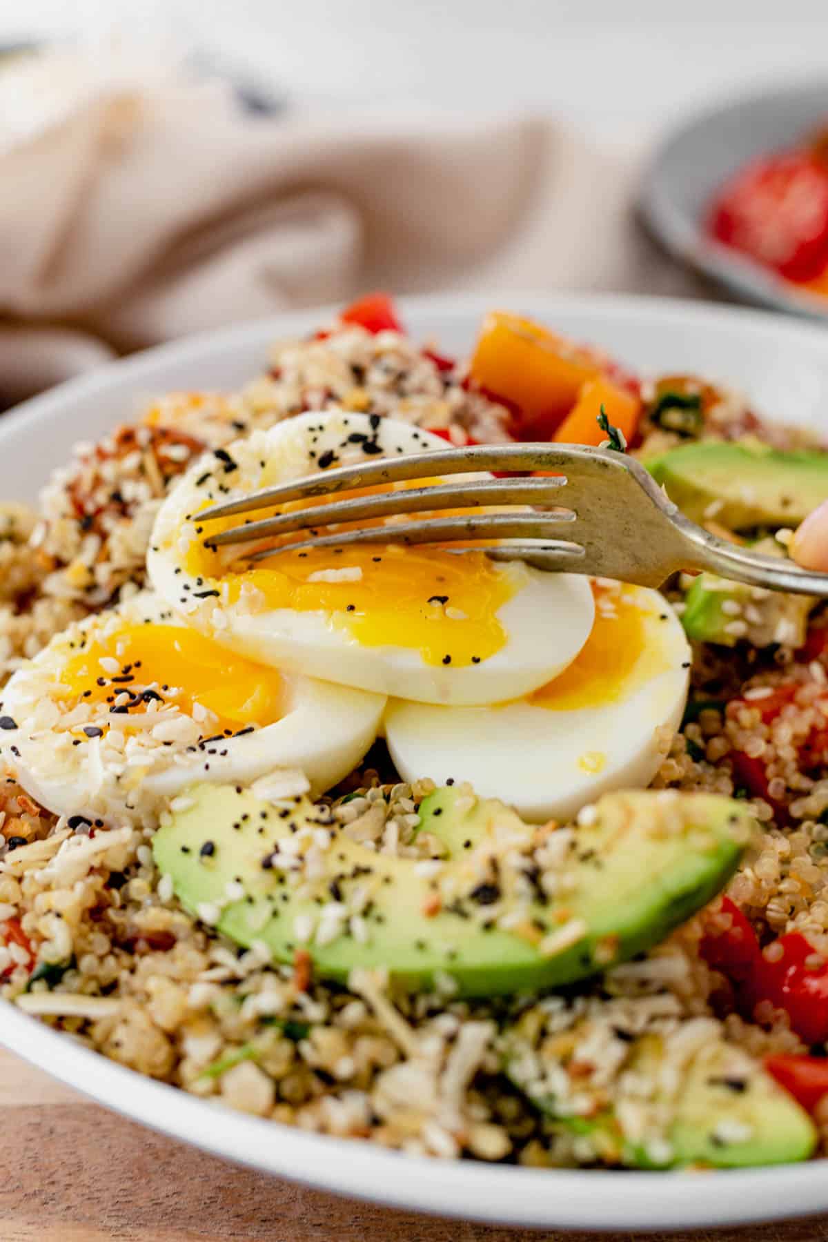 cutting into a soft boiled egg on a quinoa bowl