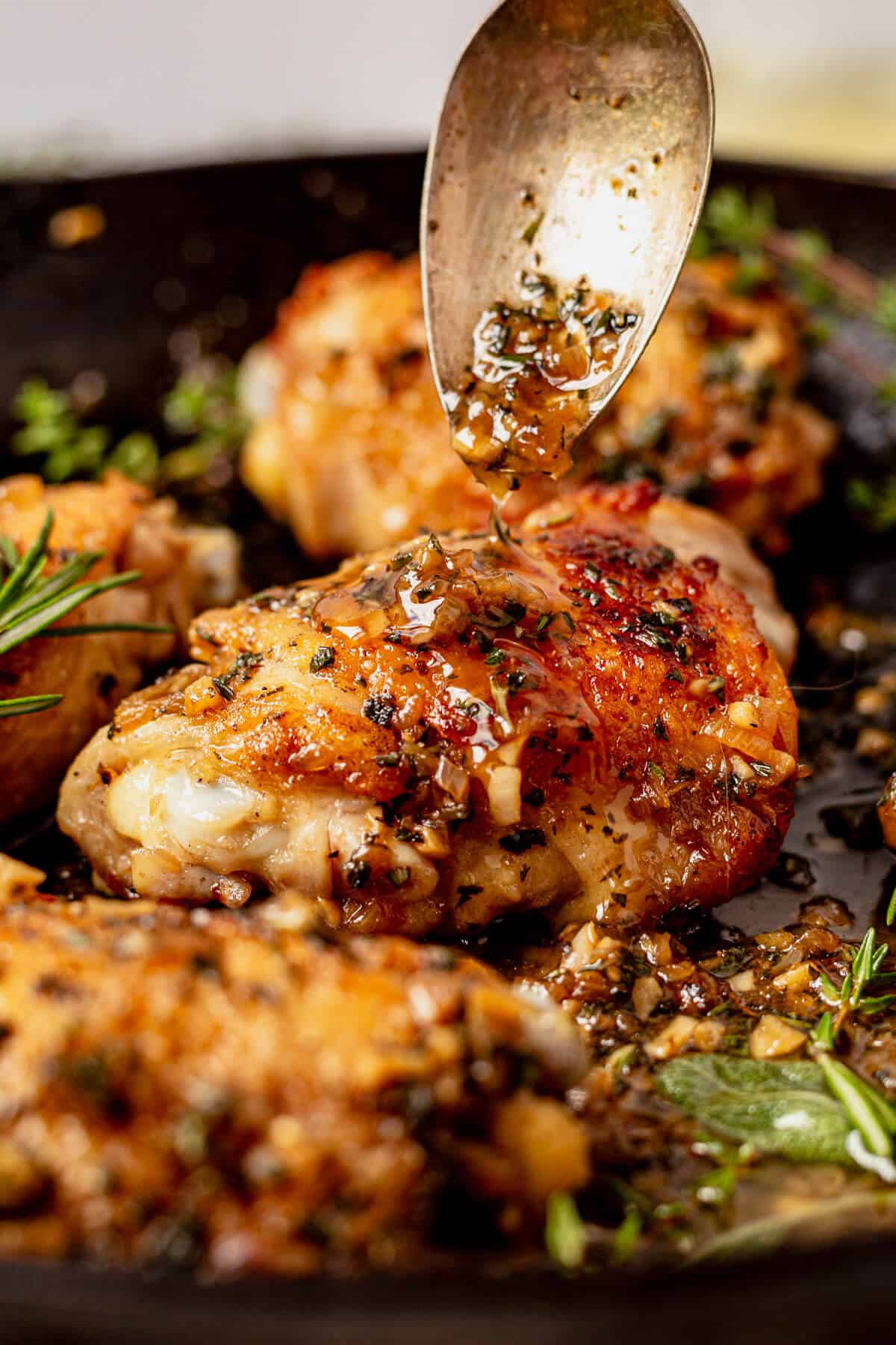 pouring herb pan sauce over a crispy chicken thigh