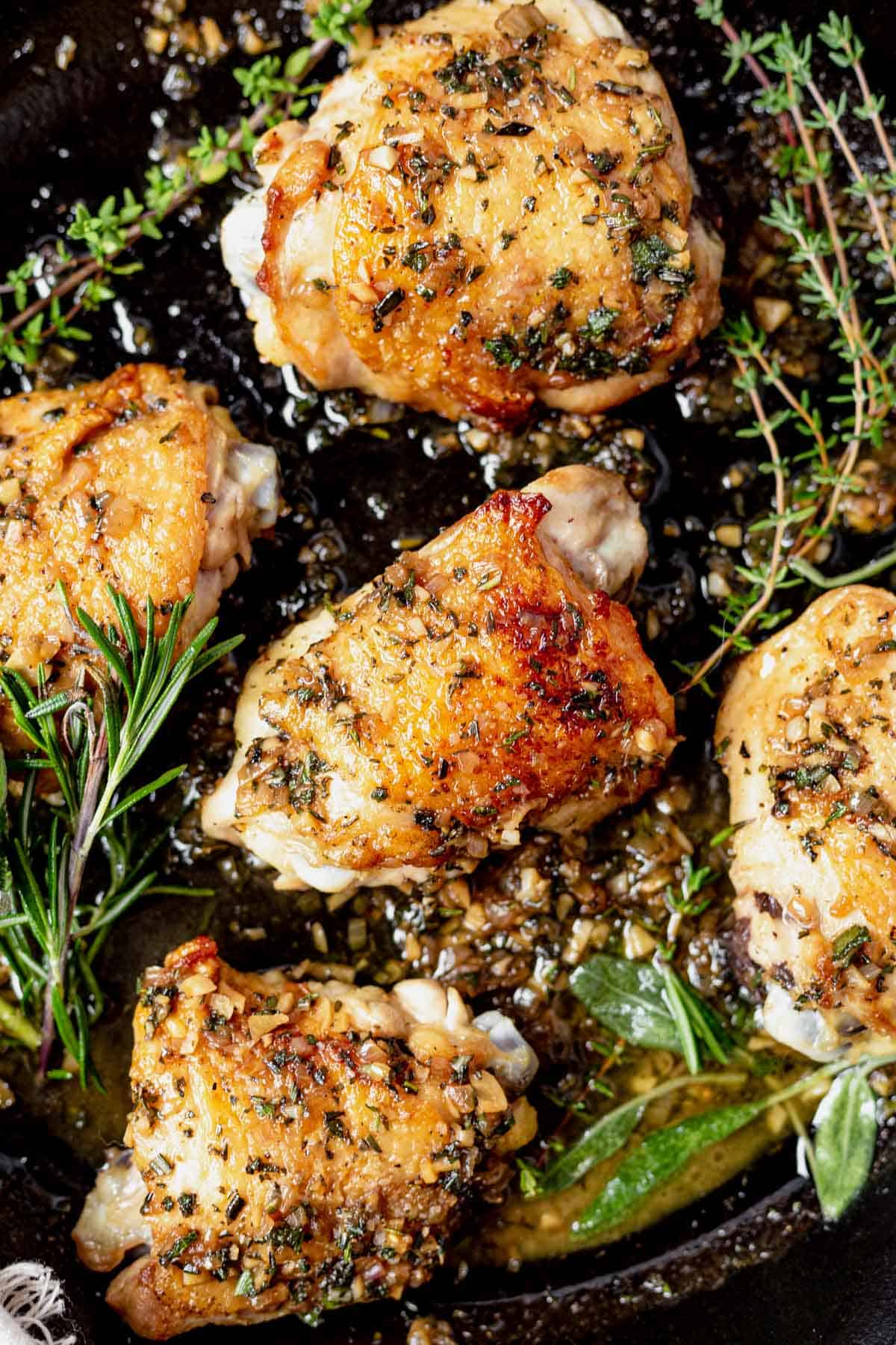 crispy chicken thighs in a cast iron skillet with sauce and fresh herbs