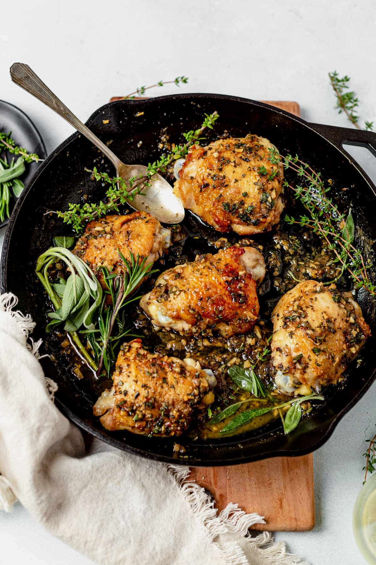 five crispy chicken thighs in a skillet with fresh herbs