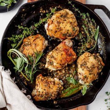 crispy chicken thighs in a cast iron skillet with fresh herbs