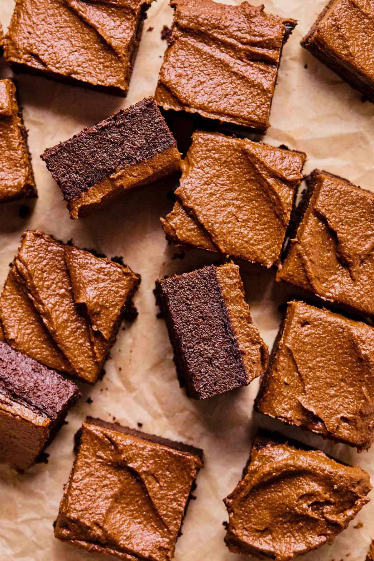 Gluten free chocolate potato with frosting cut into squares on a piece of parchment paper.
