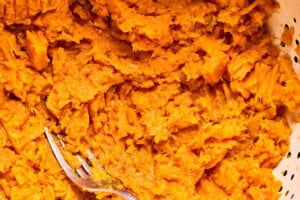 mashing cooked sweet potato in a bowl with a fork.