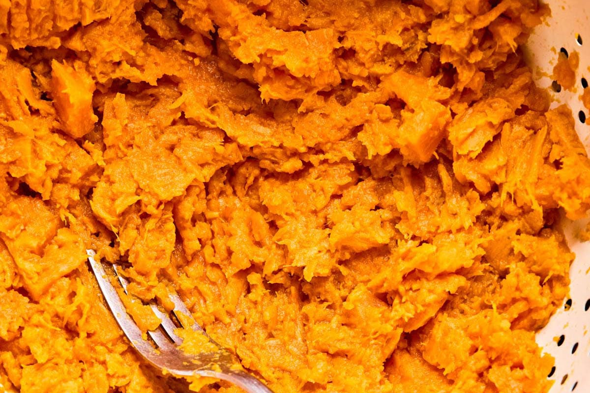 mashing sweet potatoes in a bowl with a fork.