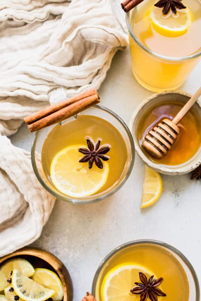 mugs of hot toddy on a countertop with a bowl of honey.