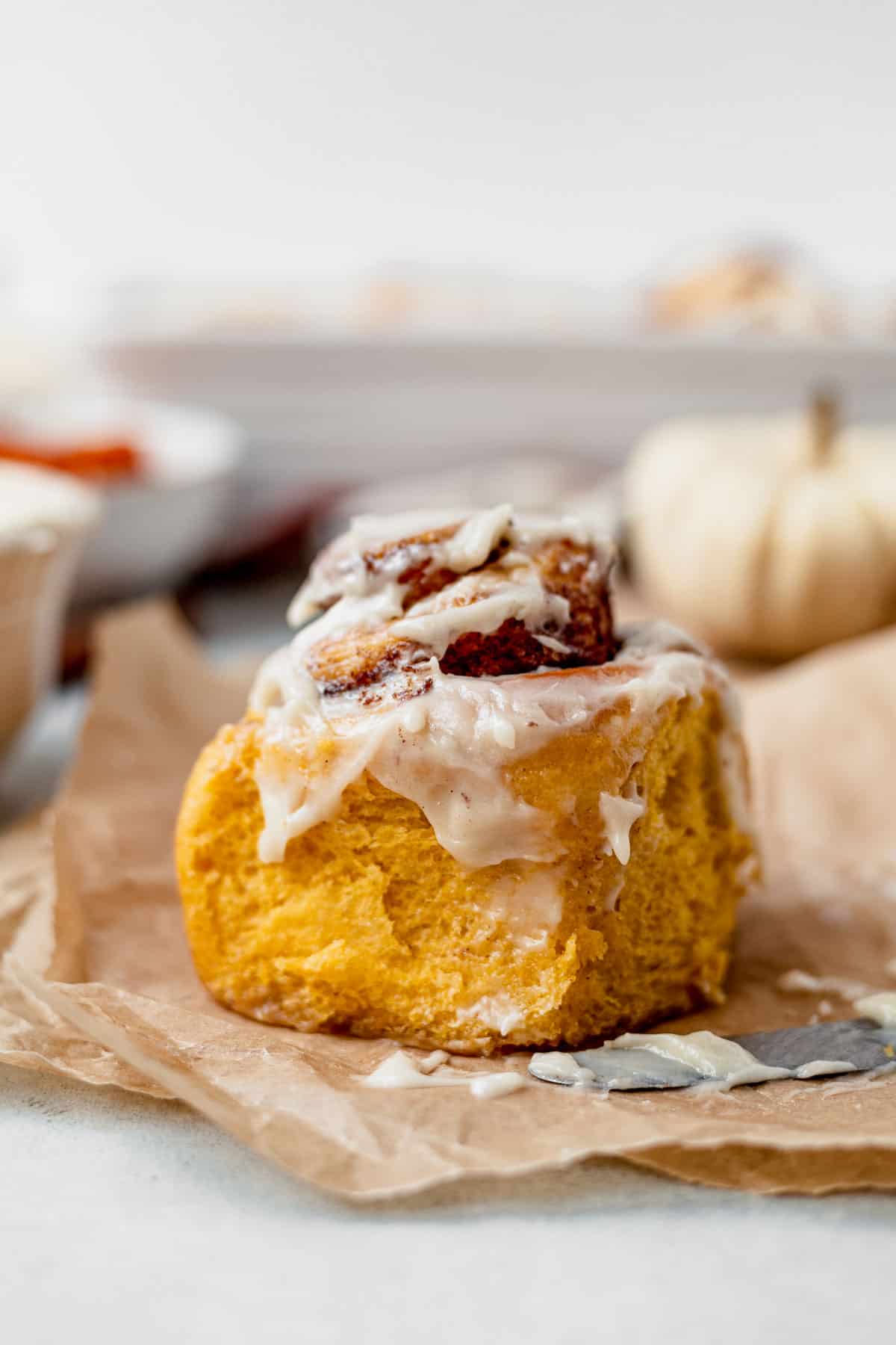 a frosted pumpking cinnamon roll on parchment paper