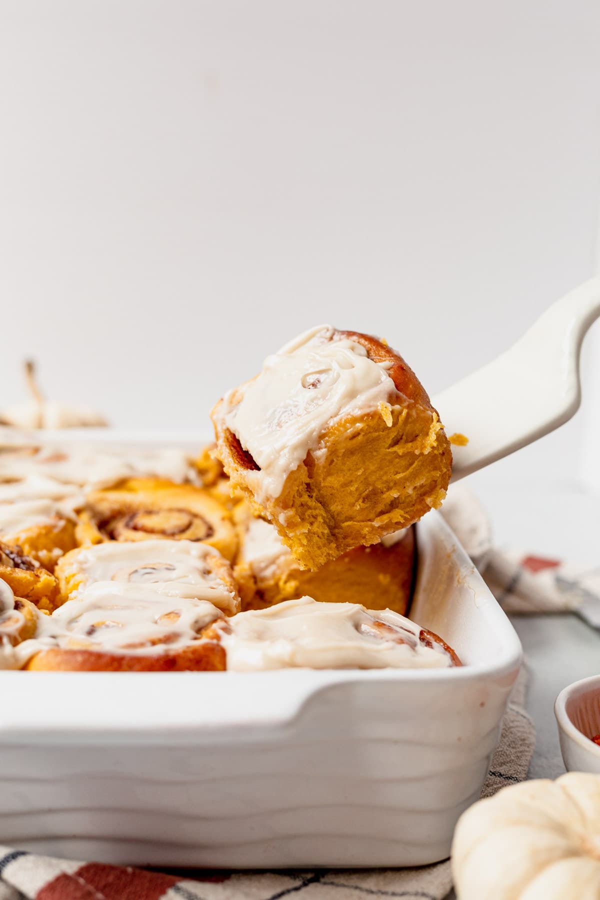 pulling a pumpkin cinnamon roll out of the pan