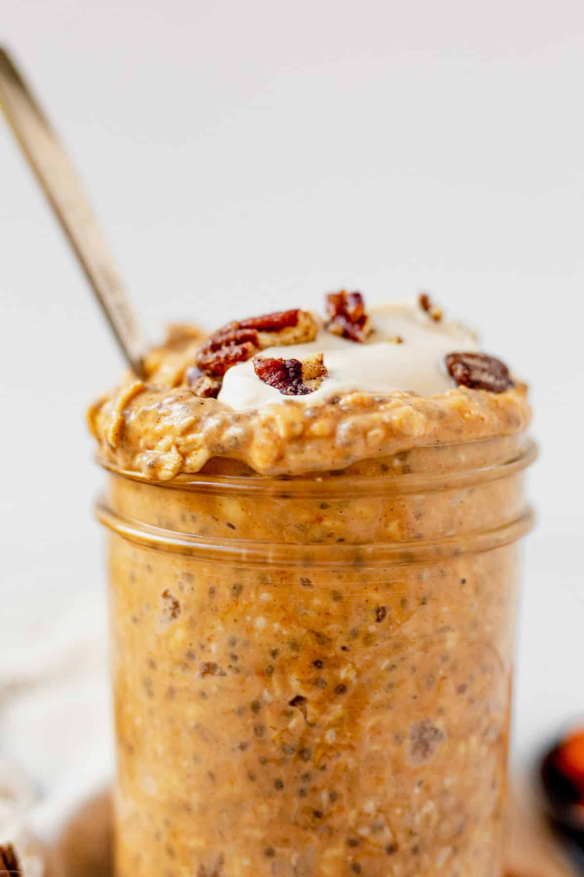 pumpkin overnight oats with yogurt and pecans spilling out of the top of a mason jar