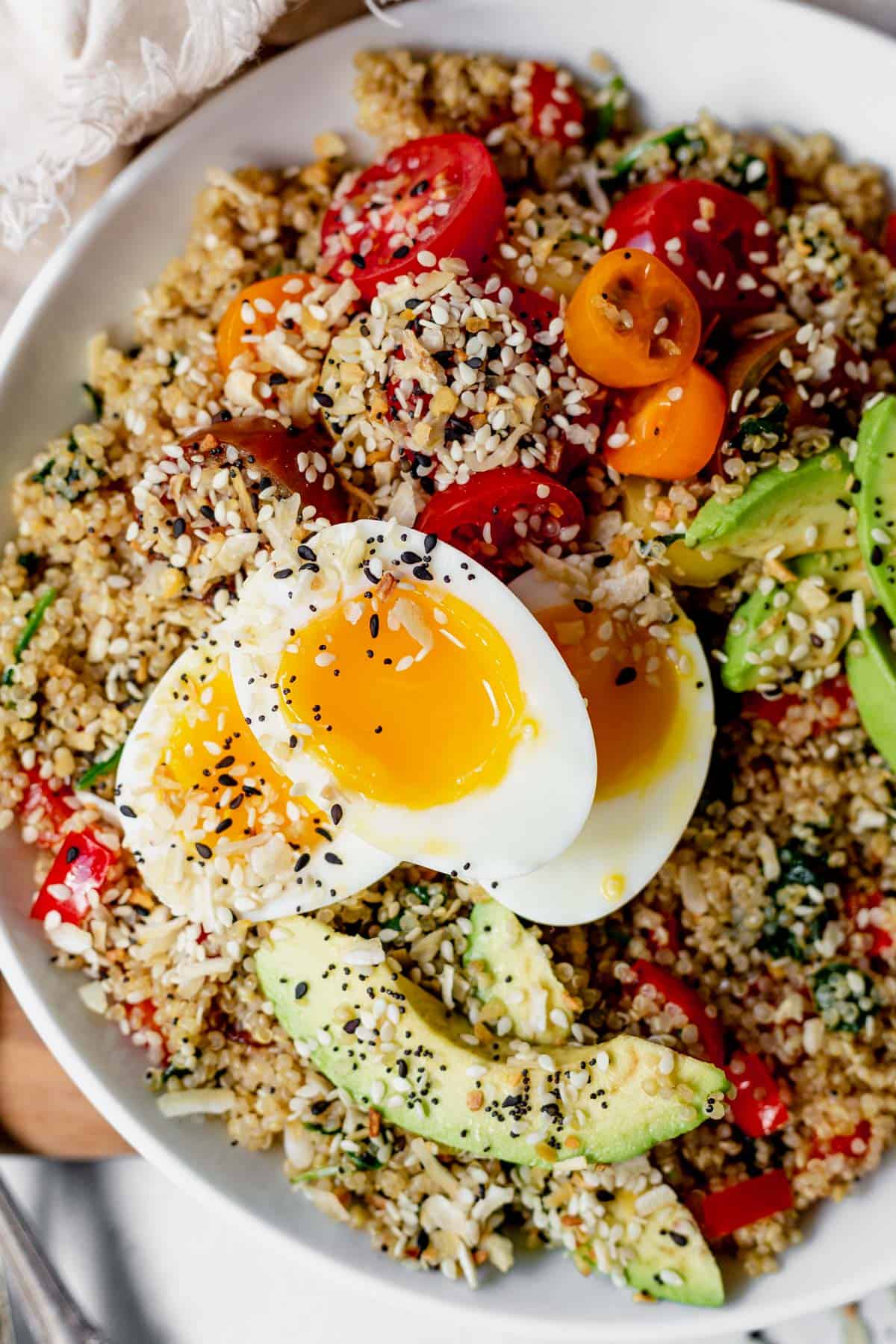 quinoa in a bowl with suateed veggies, avocado, tomato and eggs
