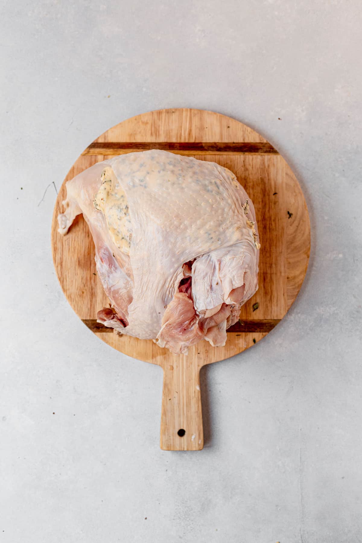 herb butter under the skin of a bone in turkey breast on a cutting board.