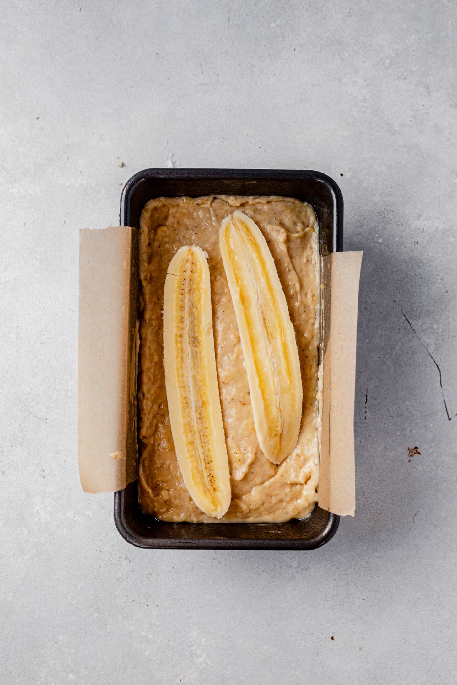 banana bread batter in a loaf pan with a slice of banana on top