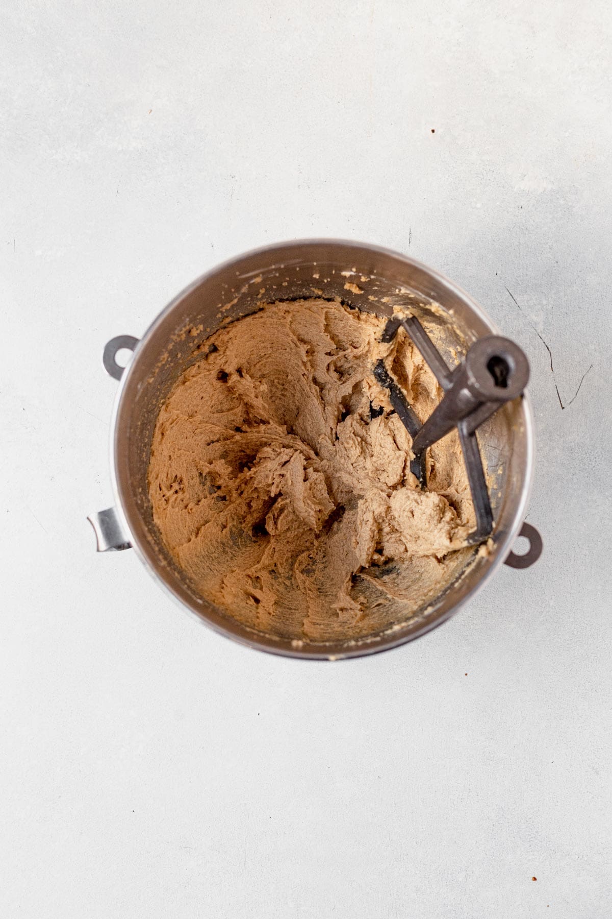 dough for caramel cheesecake cookies mixed together in a bowl with a paddle attachment.
