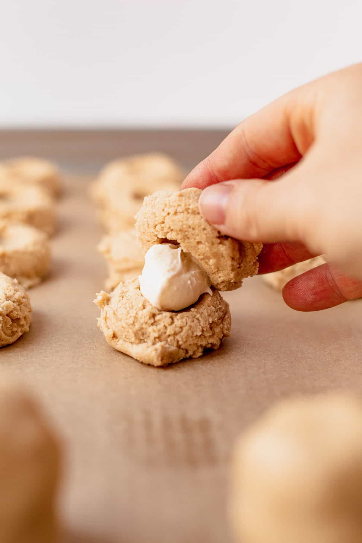 tops and bottoms of caramel cheesecake cookie dough being sandwiched together with a ball of icing in the middle.