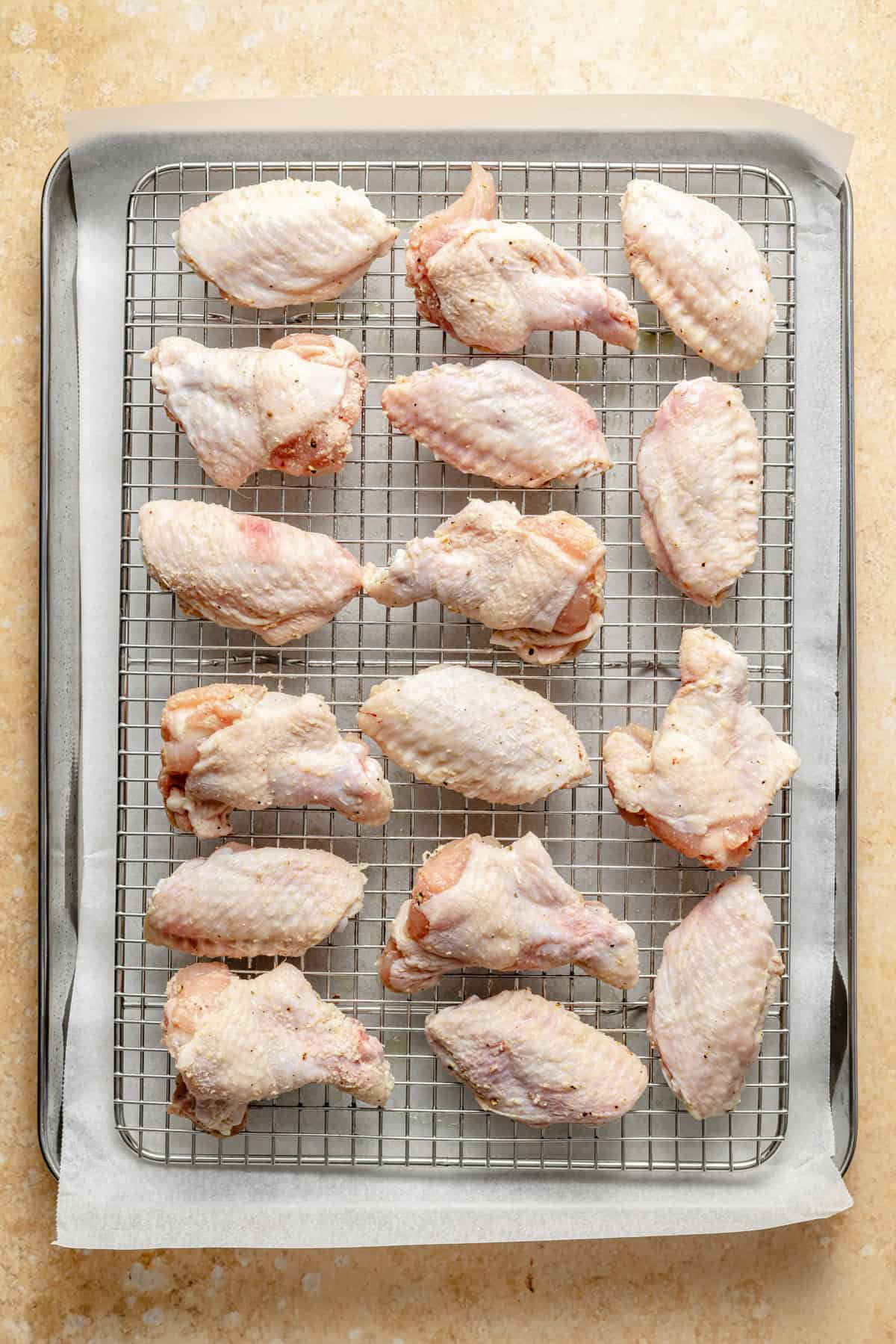raw chicken wings coated in spices and baking powder on a large sheet pan.