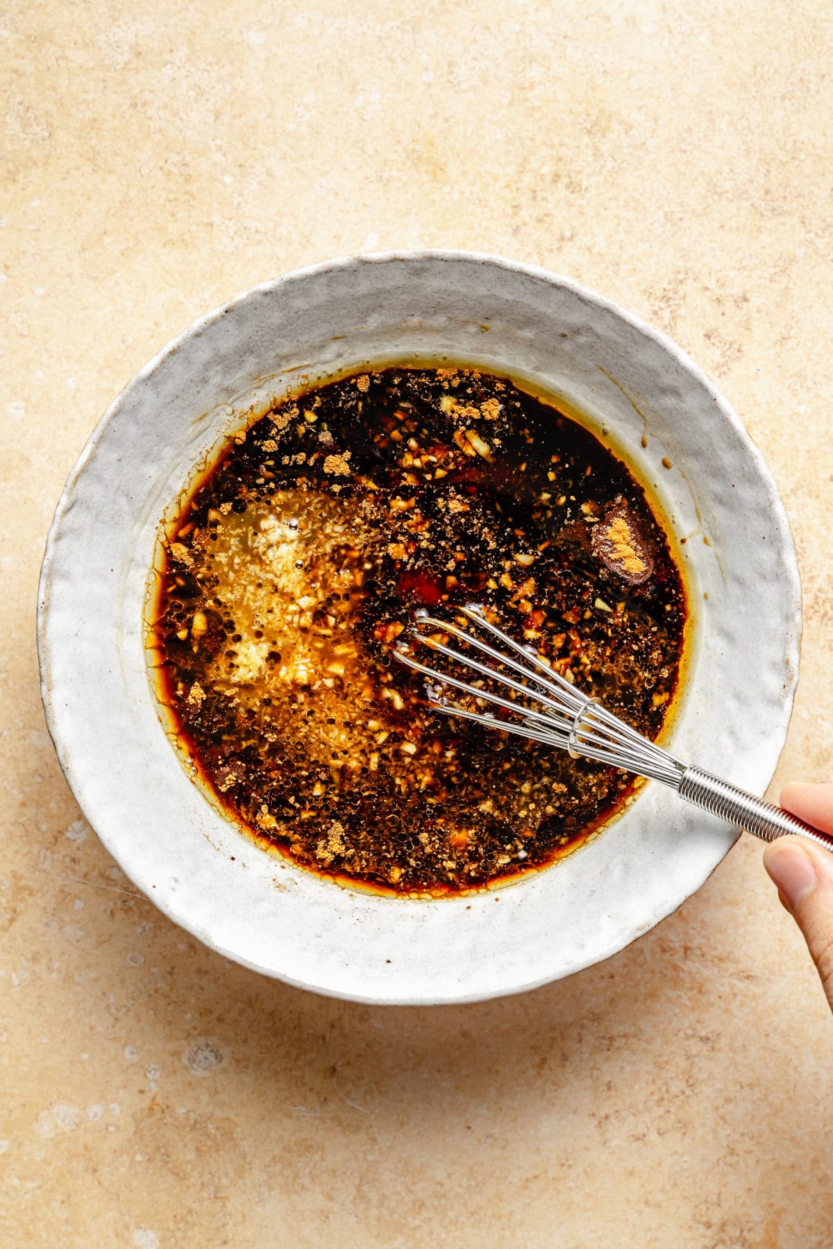 whisking a sticky asian sauce in a white bowl.