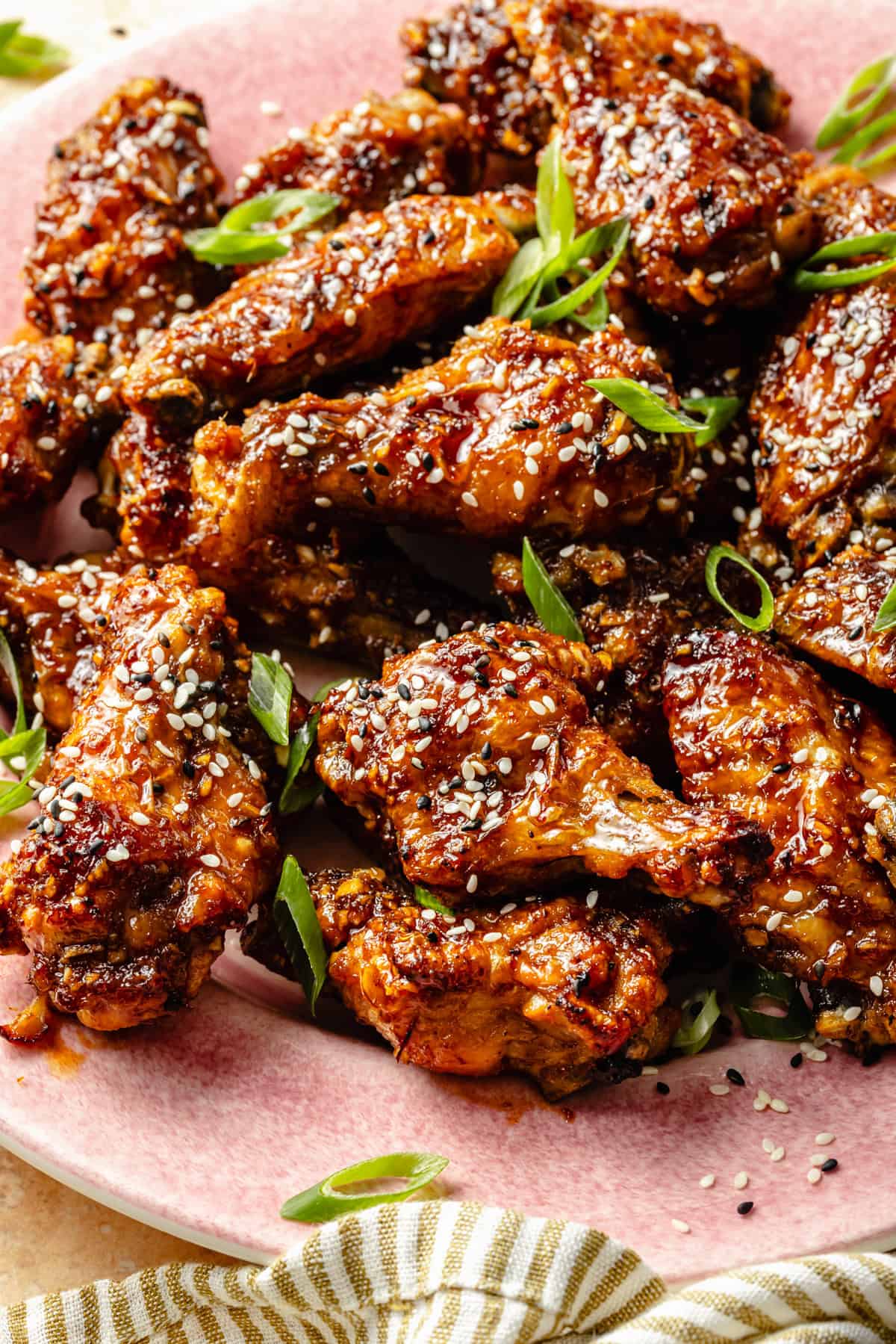 a batch of sticky glazed asian chicken wings on a plate with sesame seeds and green onions.