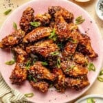 a plate of asian chicken wings topped with green onions.