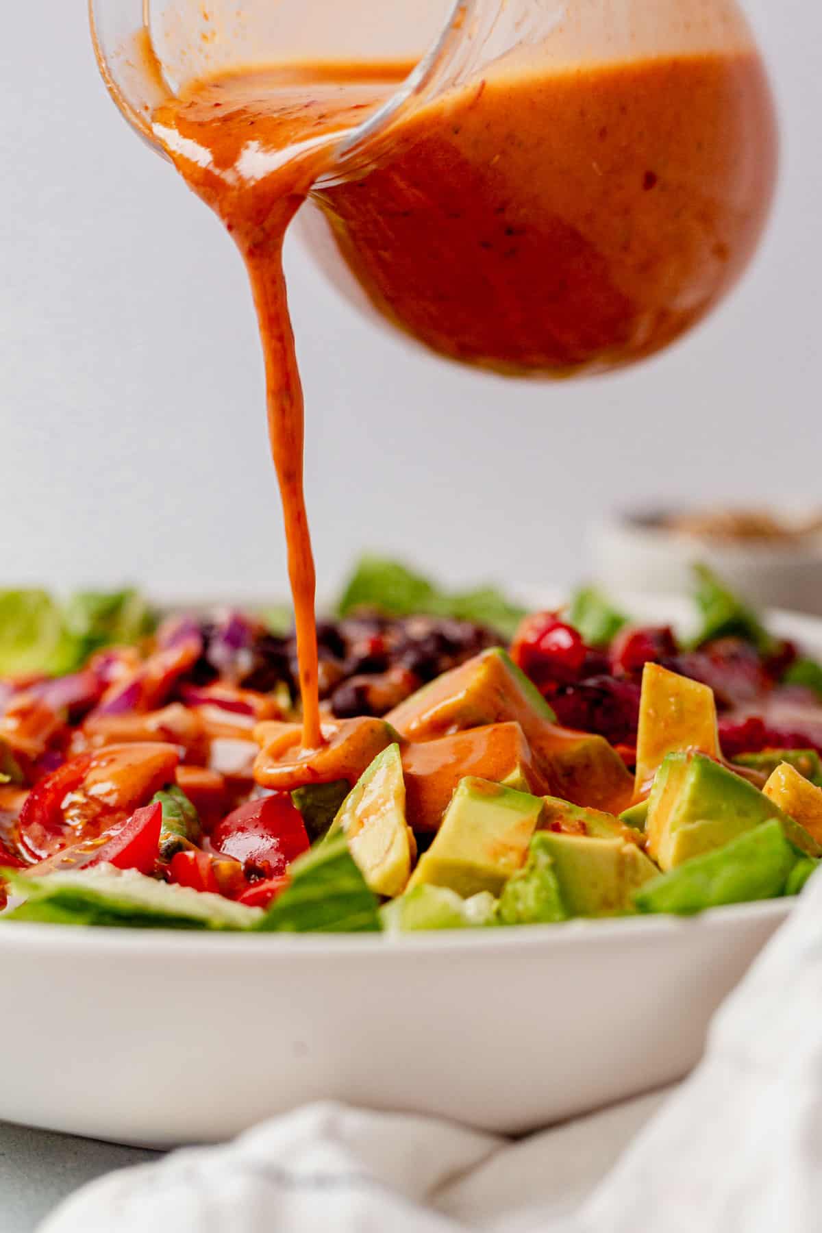 pouring chipotle honey vinaigrette over a salad with avocado, romaine, peppers, and black beans