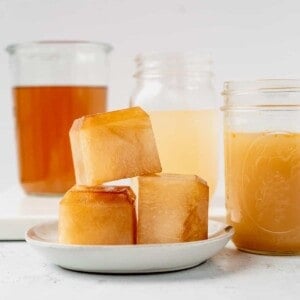 frozen chicken broth in ice cubes and fresh chicken broth in glass jars