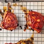 baked marinated bbq chicken thighs on a wire rack on a sheet pan.