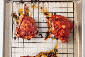 baked marinated bbq chicken thighs on a wire rack on a sheet pan.