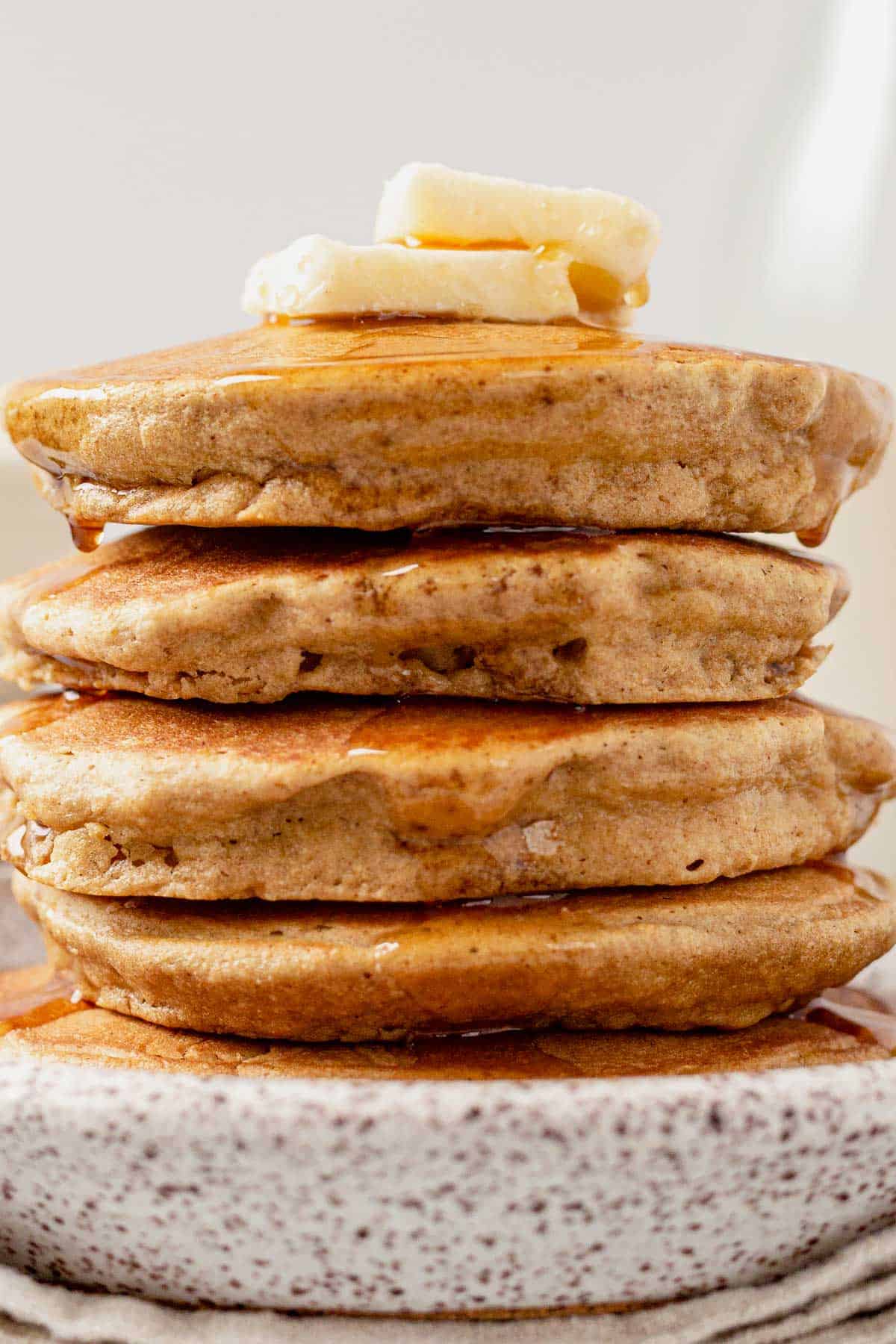 5 oat flour pancakes stacked on a plate with butter