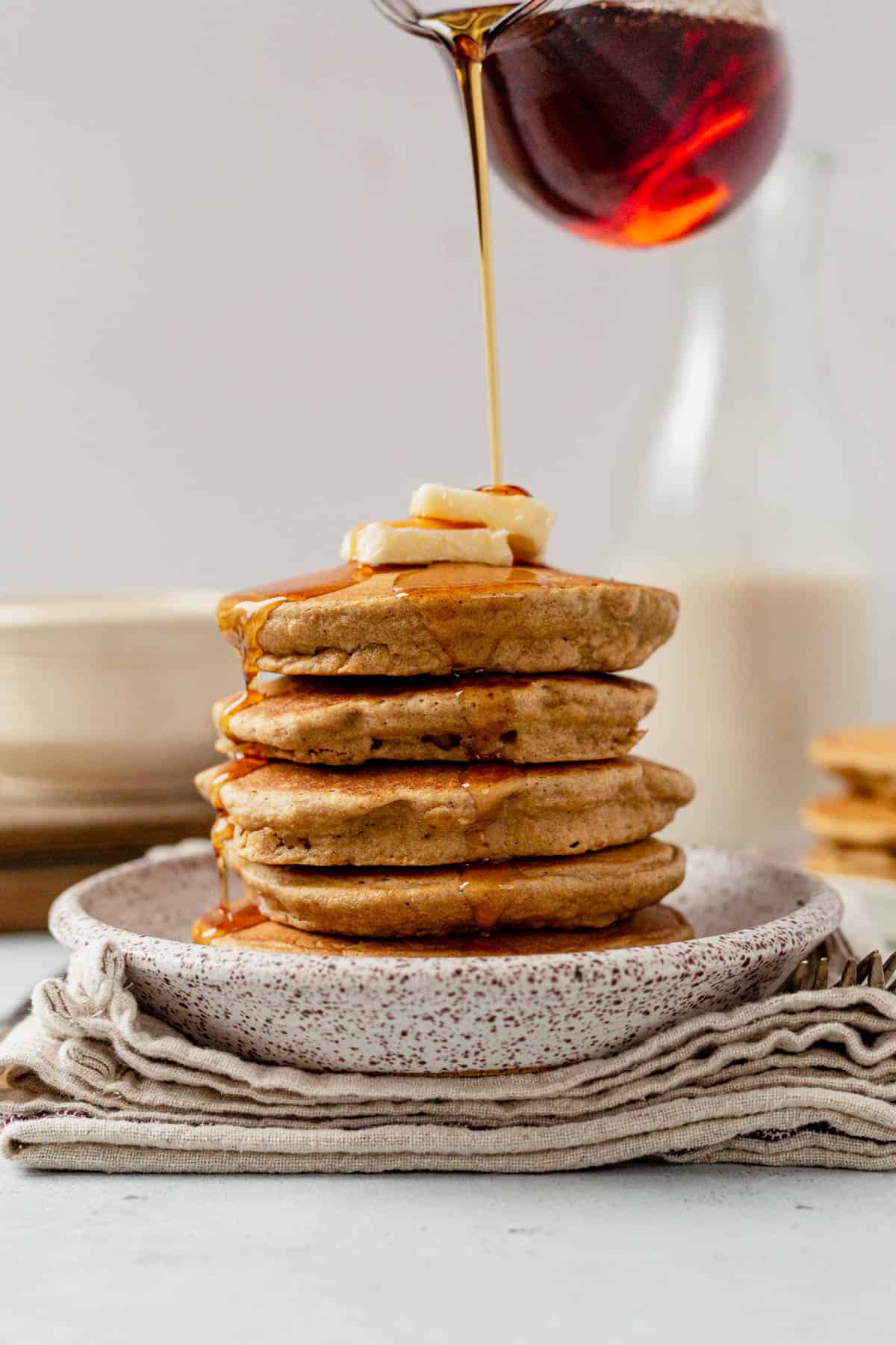 pouring syrup over a stack of oat flour pancakes