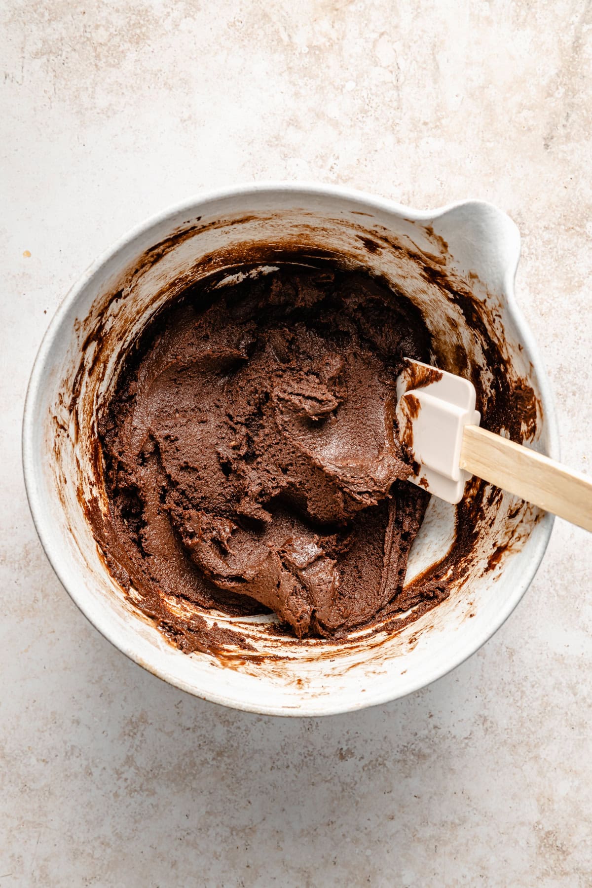 stirring edible brownie batter in a bowl with a rubber spatula.