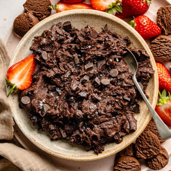 edible brownie batter in a bowl with fresh strawberries and chocolate cookies spread around it.