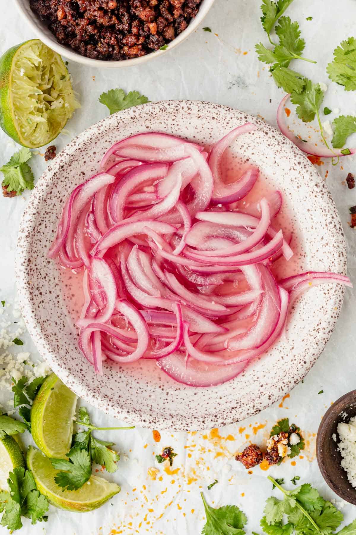 a bowl of mexican pickled onions in a bowl with ground pork tacos on the side