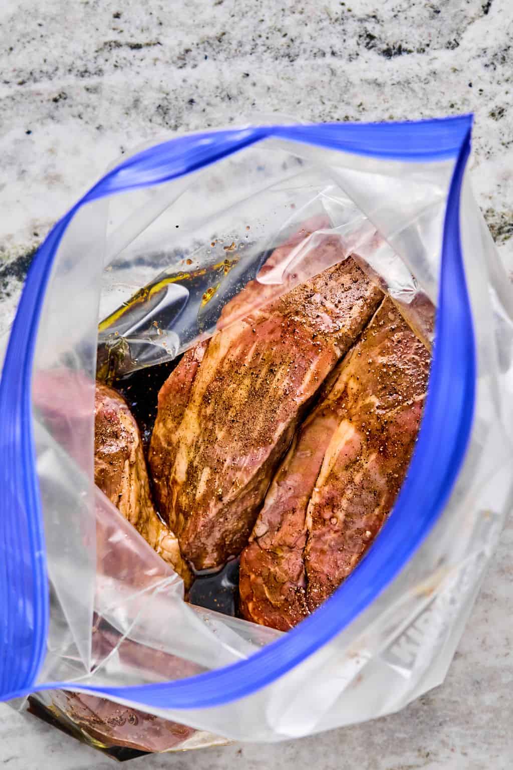 Three marinated steaks are shown inside a clear plastic zip-top bag, resting on a light-colored countertop—perfect for pairing with your favorite steak pasta dish.